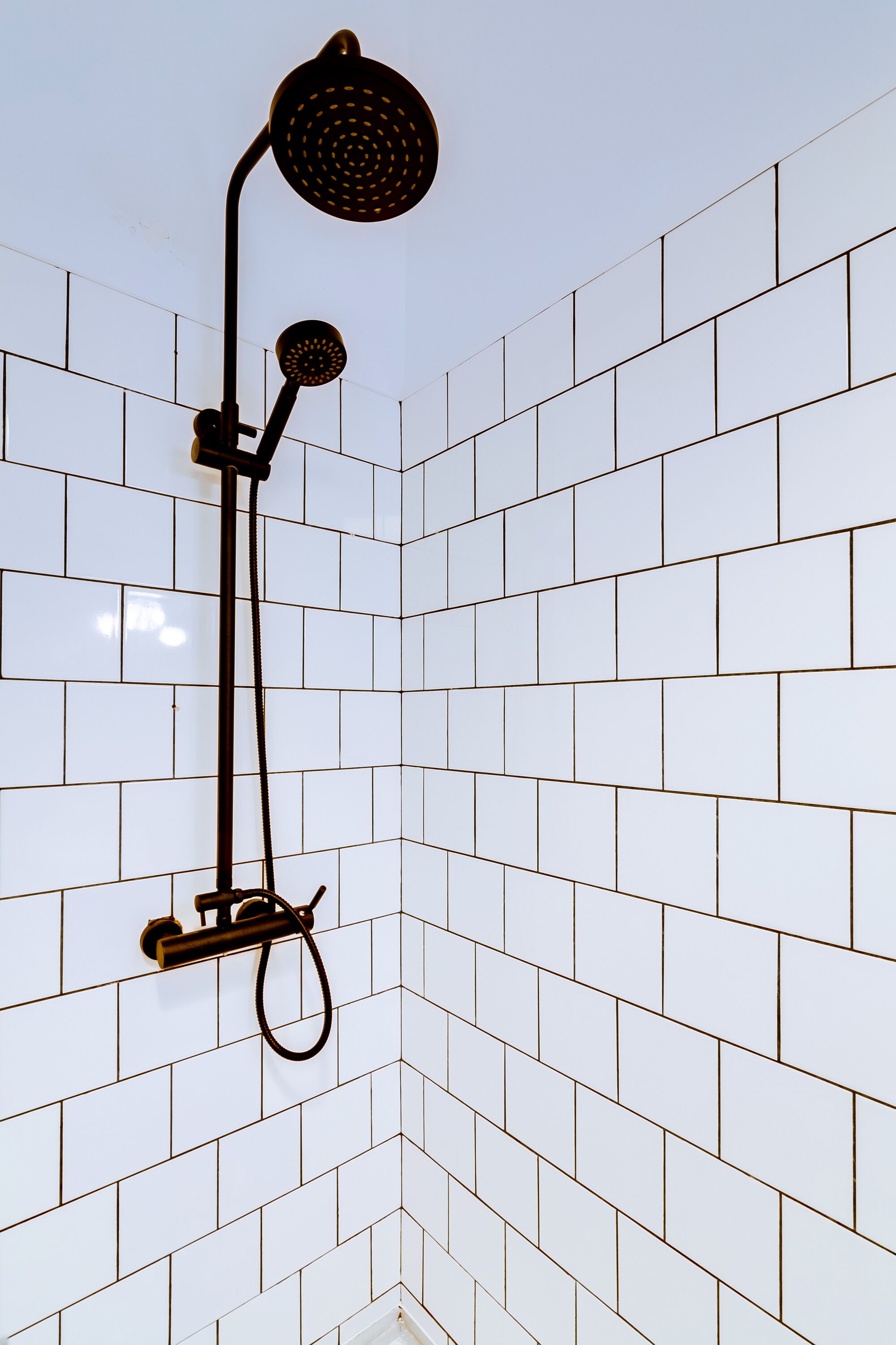 Eine Dusche mit schwarzem Schlauch und Duschkopf, an einer gefliesten Wand befestigt.