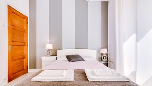 A neatly made bed with white linens and two towels, a wooden door, a nightstand with a lamp, and a bedside table with a coffee maker. - À da Avó - The Guesthouse (Faro)