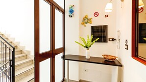 Uma escadaria com porta de vidro que dá para um quarto com uma mesa consola preta, um vaso com plantas verdes e um objeto decorativo na parede.