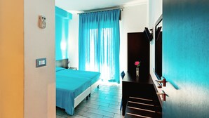 Quarto com cama, escrivaninha, cadeira, televisão e janela com cortinas.