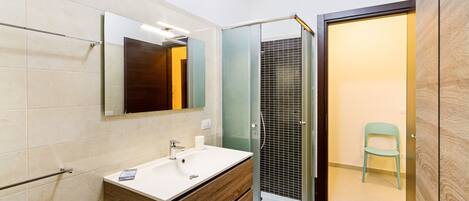 A modern bathroom with a wooden vanity, a glass shower enclosure, and a mirror above the sink.