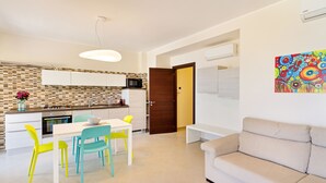 A modern kitchen with white cabinets, a microwave, and a dining area with a white table and colorful chairs.