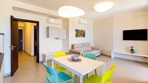 A modern living room with a dining area, a sofa, a TV, and a colorful artwork on the wall.