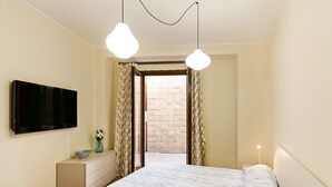A bedroom with a bed, a dresser, a TV, and a view of a brick wall through a doorway.