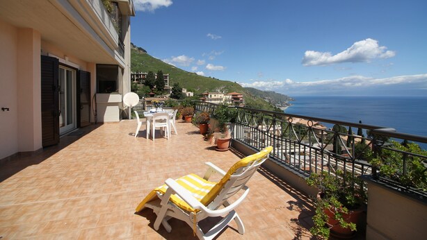 A balcony with a yellow-striped lounge chair, a table, and potted plants. - Fontana Vecchia Seaview Apartment  (Taormina)