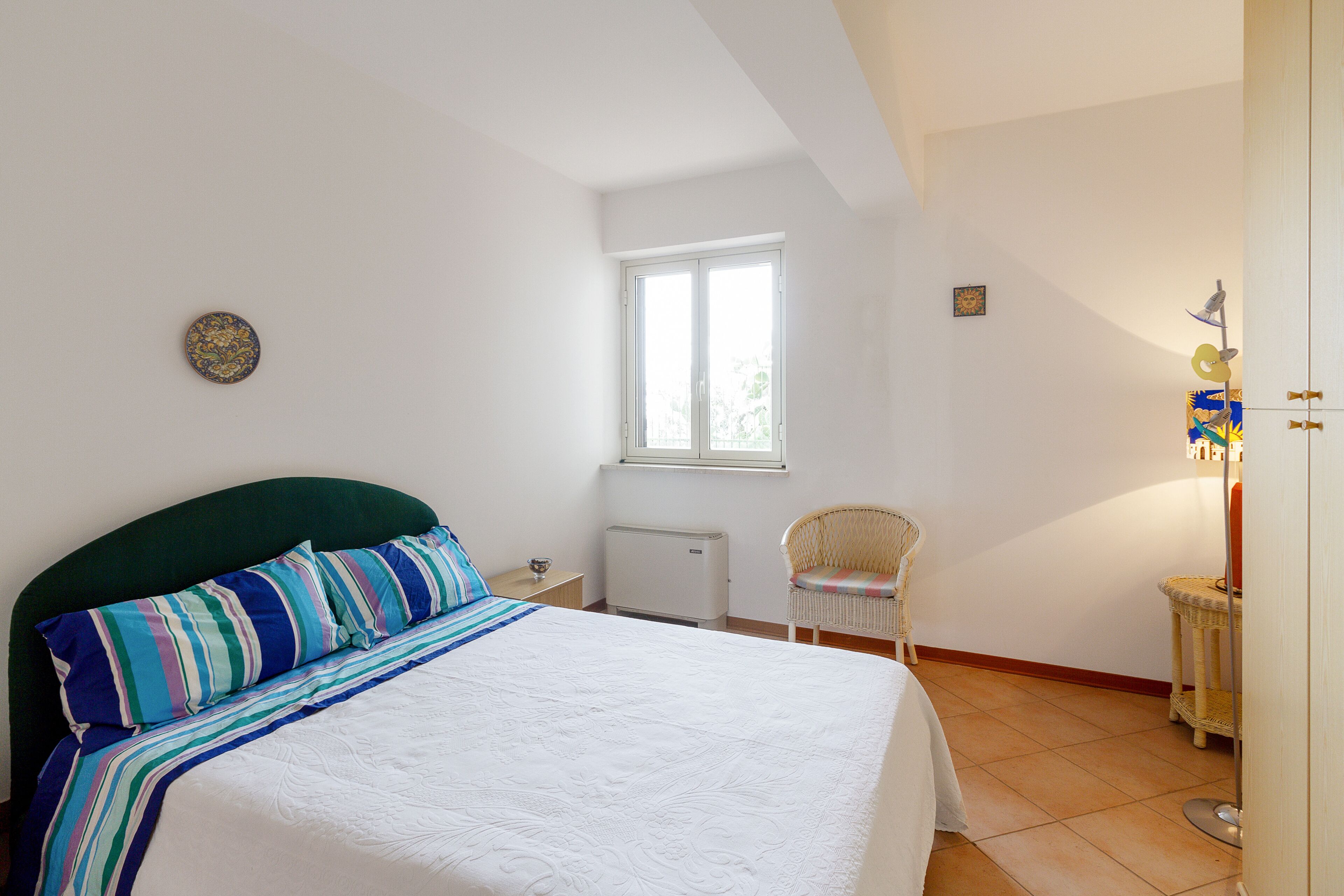 A bedroom with a bed, a window, a radiator, a chair, and a small table.