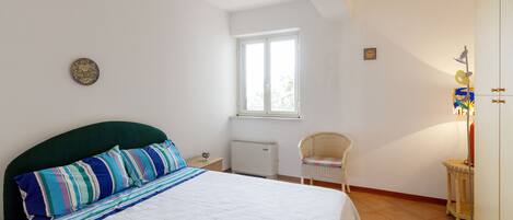 A bedroom with a bed, a window, a radiator, a chair, and a small table.