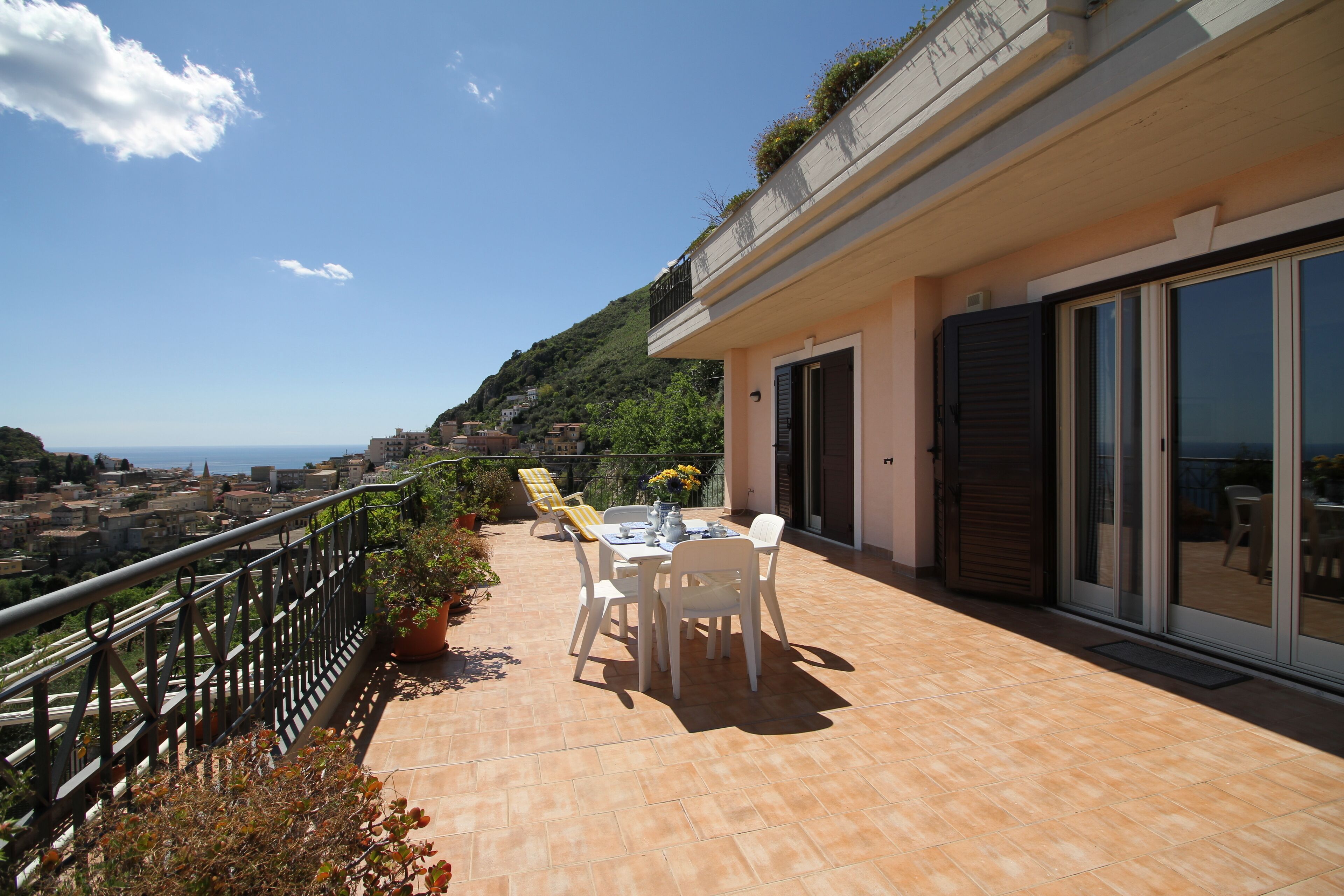 A balcony with a table and chairs, overlooking a coastal town.