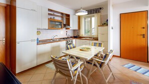 A compact kitchen with white cabinets, a dining table with chairs, and a wooden door. - Fontana Vecchia Seaview Apartment  (Taormina)