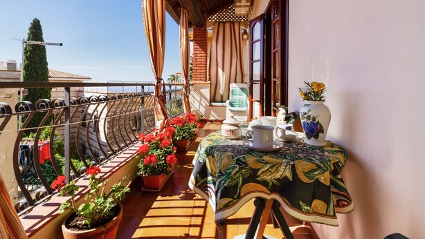 A balcony with potted plants, a table with a tablecloth, and a chair. - Taormina Vintage Loft  (Taormina)