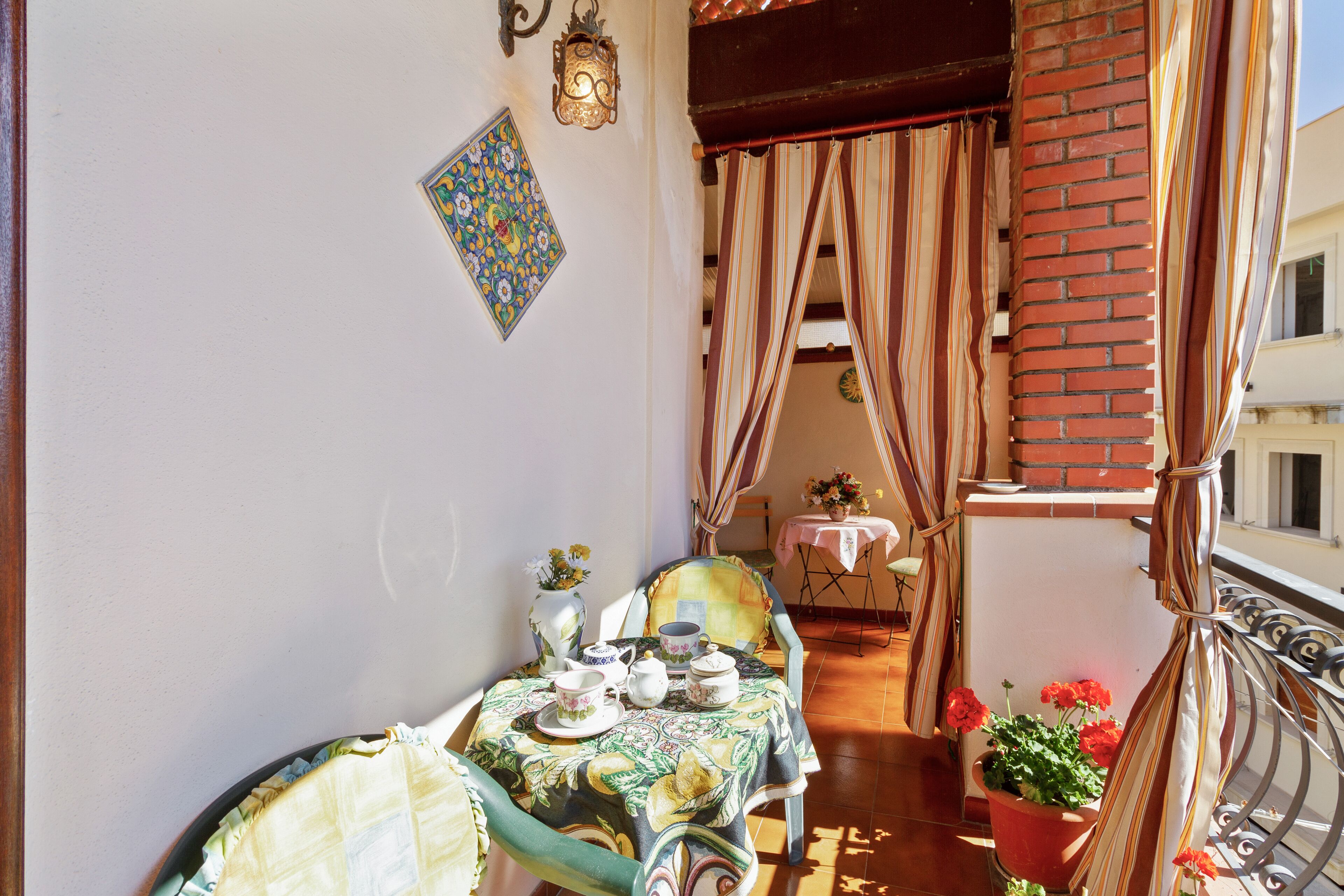 A balcony with a table set for tea, a chair, a potted plant, and a view of the street.