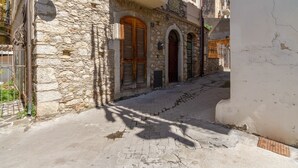 A narrow cobblestone street flanked by stone buildings with wooden shutters and balconies. - Taormina Vintage Loft  (Taormina)