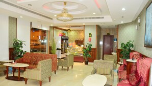 A hotel lobby with a red sofa, patterned armchairs, a coffee bar, and a chandelier. - Quiet Rooms 3 (Riyadh)