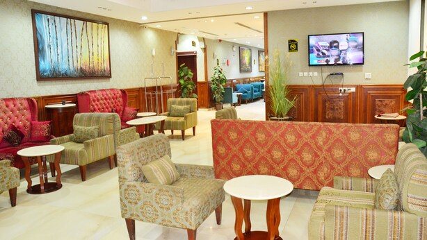 A hotel lobby with multiple seating areas, a television, and a large painting on the wall. - Quiet Rooms 3 (Riyadh)