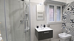 A modern bathroom with a glass-enclosed shower, a white sink with a dark cabinet, and a bidet. - R&B San Rafèl (Bologna)
