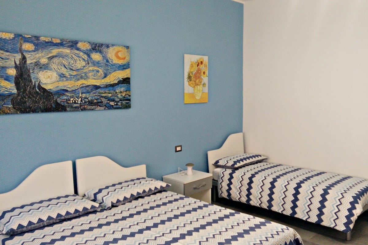 A room with two beds, a nightstand, a wall painting, and a door.