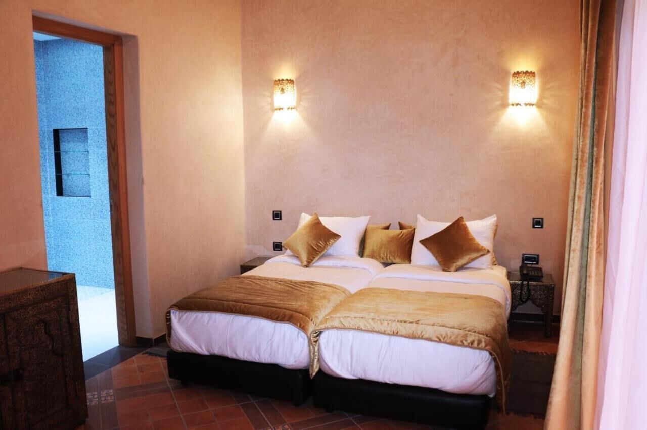 Uma cama de casal com duas almofadas, uma mesinha de cabeceira e uma luminária fixada na parede.