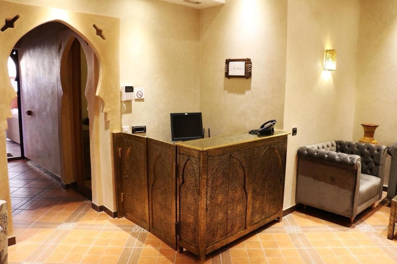 Zona de recepción con un mostrador de madera, un teléfono negro, un certificado enmarcado en la pared y un sofá gris.