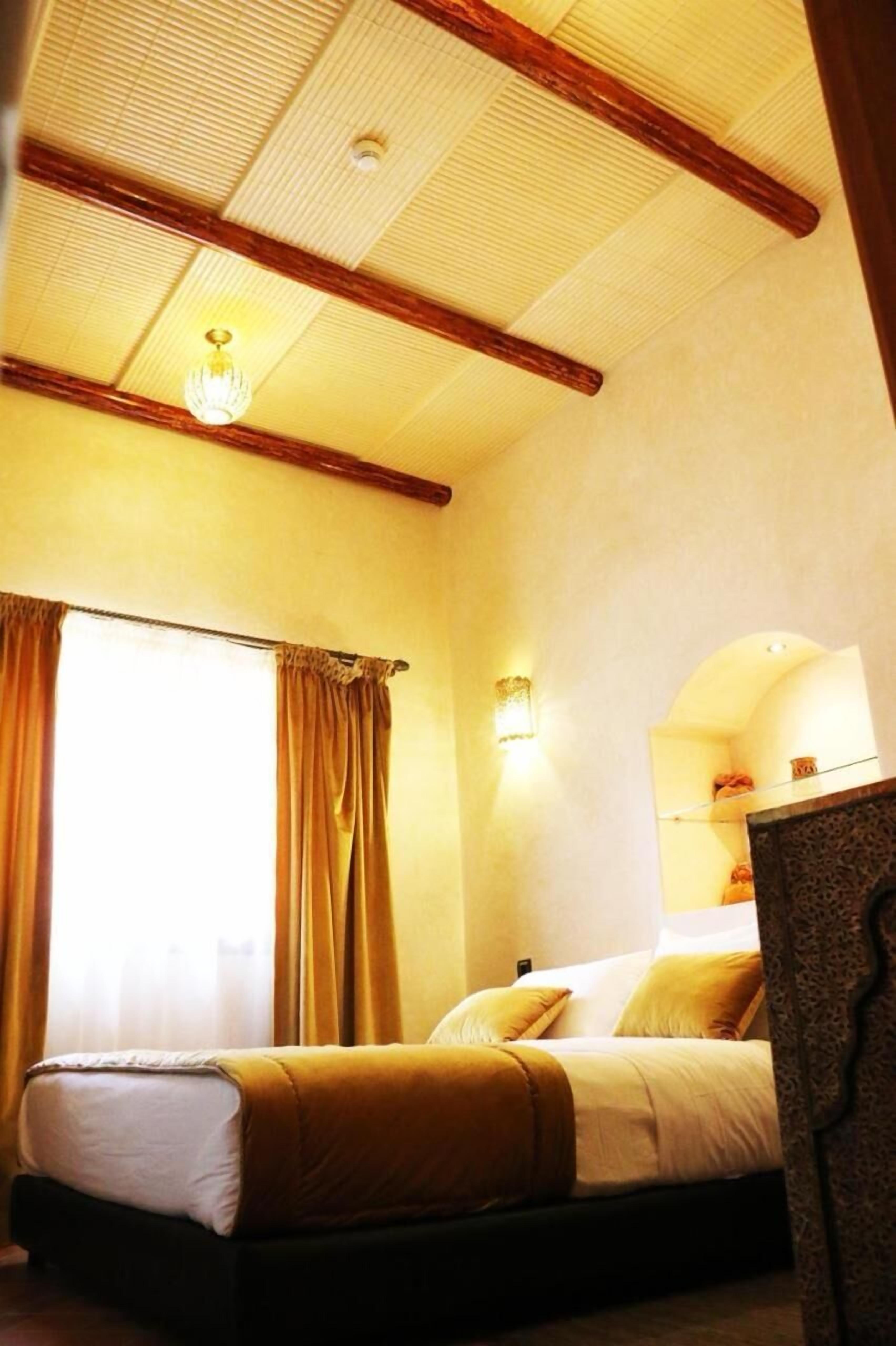 A hotel room with a bed, curtains, a chandelier, and a wall-mounted light fixture.