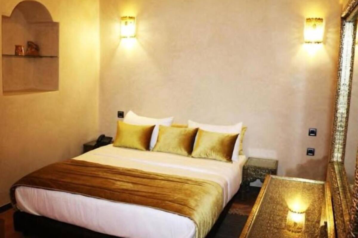 Una habitación de hotel con una cama grande, dos mesitas de noche y luces fijadas a la pared.