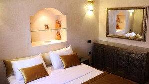 A hotel room with a bed, a nightstand, a wall-mounted shelf with decorative items, and a mirror. - Maison d'hote Dar amghar (Tafraout)
