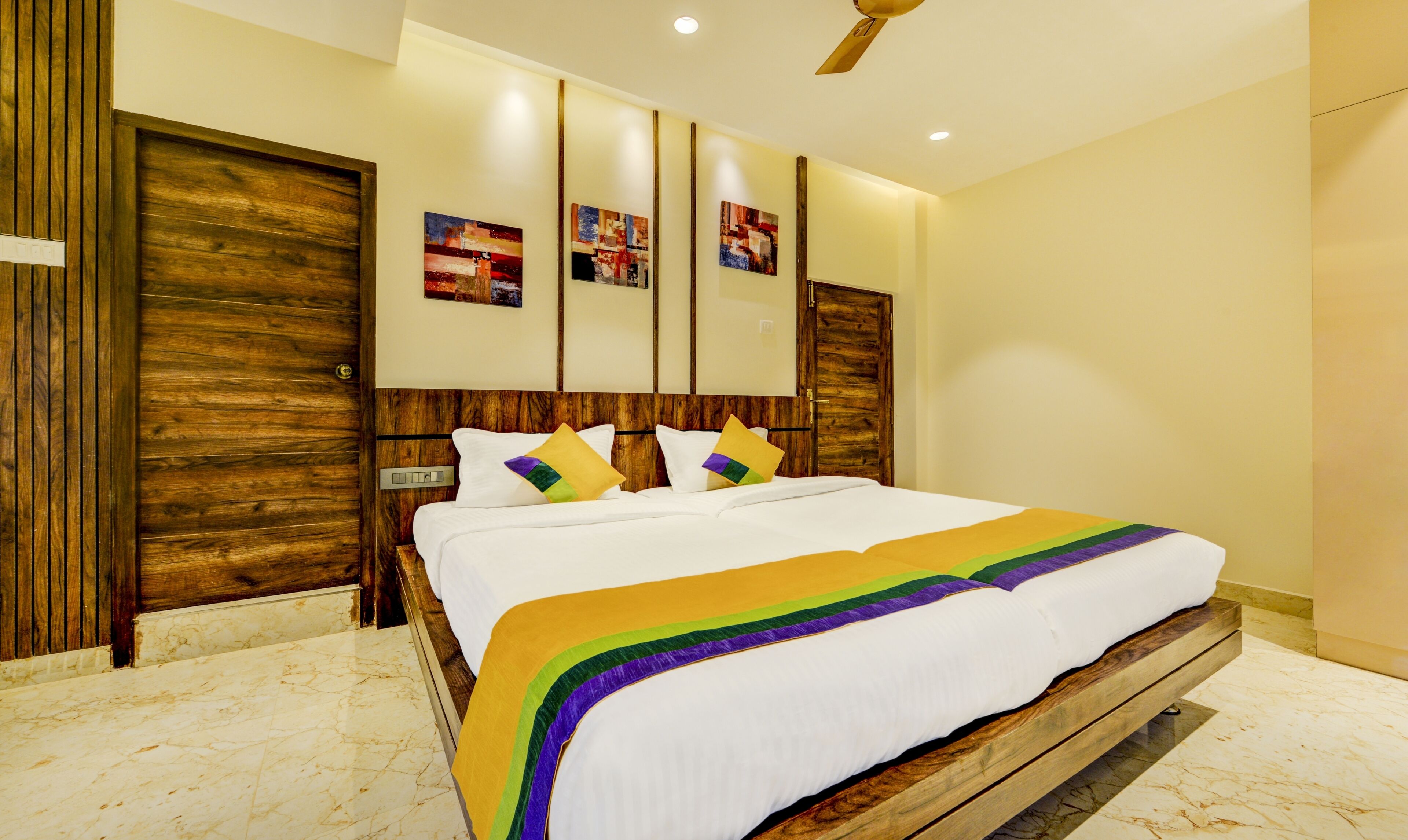 A hotel room with a large bed, wooden headboard, and three wall-mounted artwork pieces.