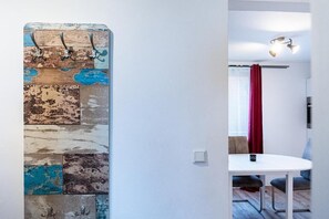 A room with a white wall, a wooden wall decoration with metal hooks, a white round table, and a red curtain. - Witte Kliff Helgoland (Helgoland)