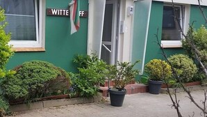 Un bâtiment à la façade verdoyante, une enseigne indiquant « WITTE OFF », et des plantes en pot devant l’entrée.