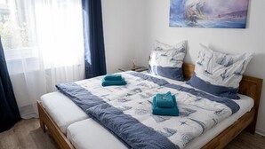 Un lit bien fait, avec une courtepointe et des oreillers, un tableau accroché au mur et une fenêtre avec des rideaux.