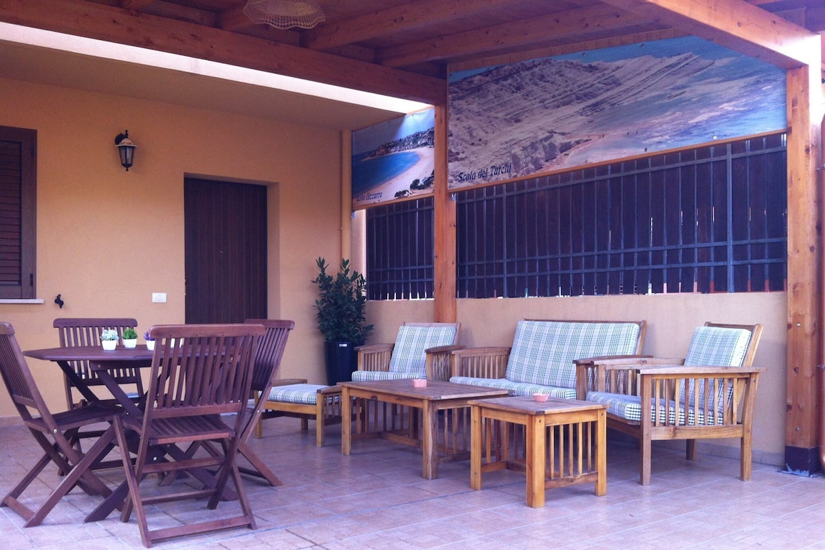 An outdoor patio with wooden furniture, including a table and chairs, and a sofa.