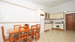 A kitchen with white tiled walls, wooden cabinets, a dining table with chairs, and a tiled floor. - Quiet retreat with pool and BBQ (Albufeira)