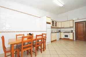 A kitchen with white tiled walls, wooden cabinets, a dining table with chairs, and a tiled floor. - Quiet retreat with pool and BBQ (Albufeira)
