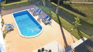 A swimming pool with lounge chairs and a table with plates, surrounded by a brick patio and a grassy area.