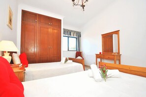 Un dormitorio con un armario grande, una mesita de noche con lámpara, un espejo y una ventana con cortinas.