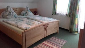 A bedroom with a wooden bed, floral bedding, a window with curtains, and a radiator. - Holidays at the Fam. Moosbrugger volgo Rainzhof (Aich)
