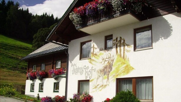 A building with a mural of a wolf and a mountain landscape, surrounded by colorful flower boxes and a well-maintained garden. - Holidays at the Fam. Moosbrugger volgo Rainzhof (Aich)