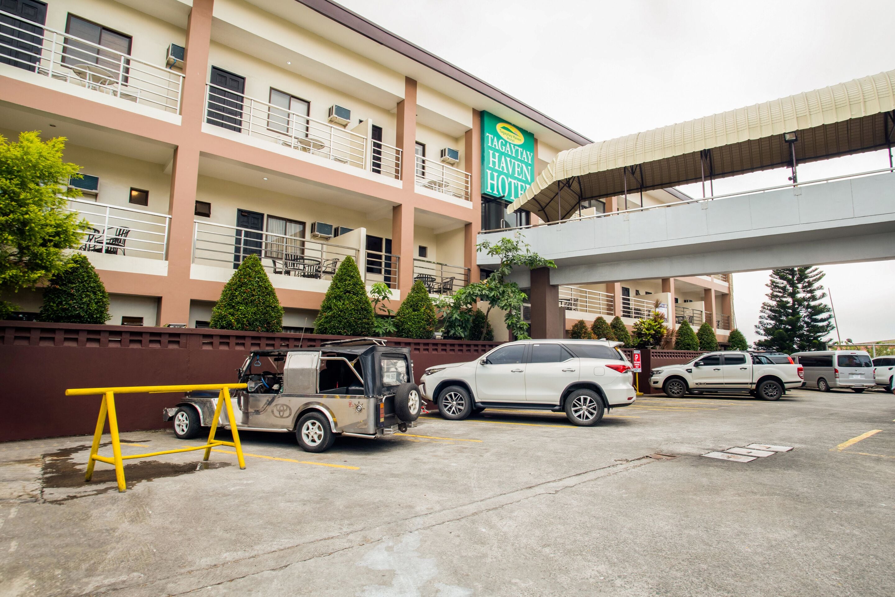 A multi-story hotel with a sign reading "Tagaytay Haven Hotel". There are several vehicles parked in the lot, including a white SUV and a pickup truck.