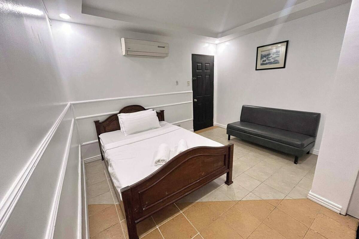 Un dormitorio con una cama de madera, un sofá gris y una puerta.
