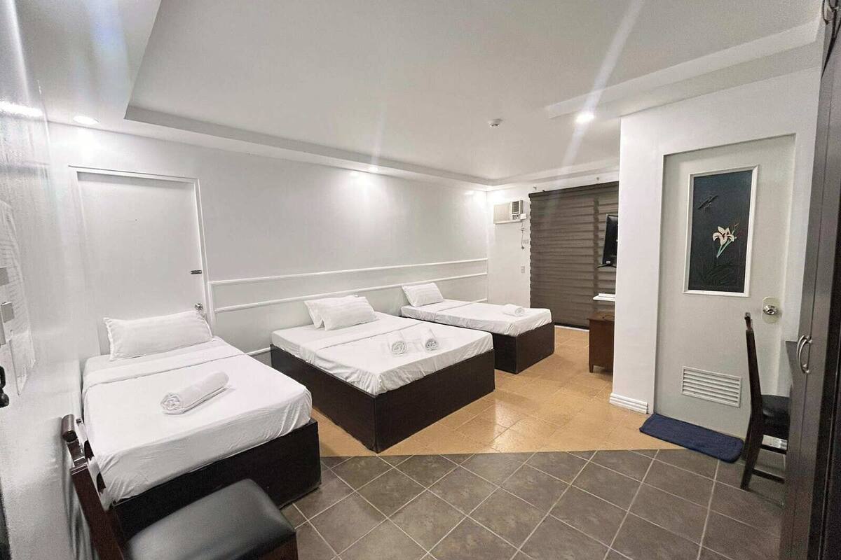 Habitación de hotel con dos camas individuales, un sofá cama, un escritorio pequeño y un baño con ducha e inodoro.