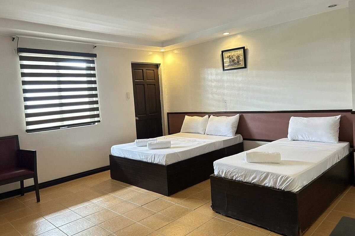 Habitación de hotel con dos camas individuales, una ventana con persianas, una puerta y un cuadro en la pared.