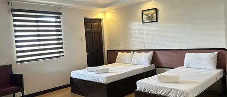 A hotel room with two single beds, a window with blinds, a door, and a framed picture on the wall.