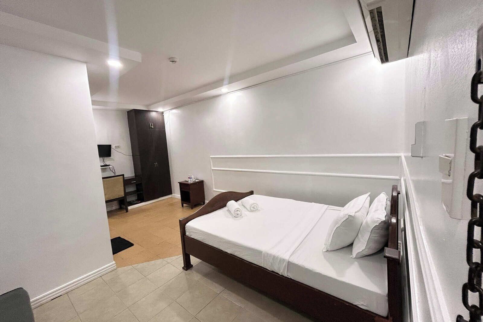 Una habitación de hotel moderna con una cama grande, un armario, un escritorio pequeño y un televisor.