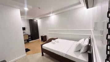 Una habitación de hotel moderna con una cama grande, un armario, un escritorio pequeño y un televisor.