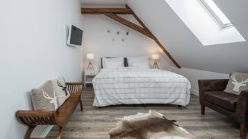 A bedroom with a sloped ceiling, a bed with a white quilt, a wooden bench, a brown sofa, and a fur rug on the floor.