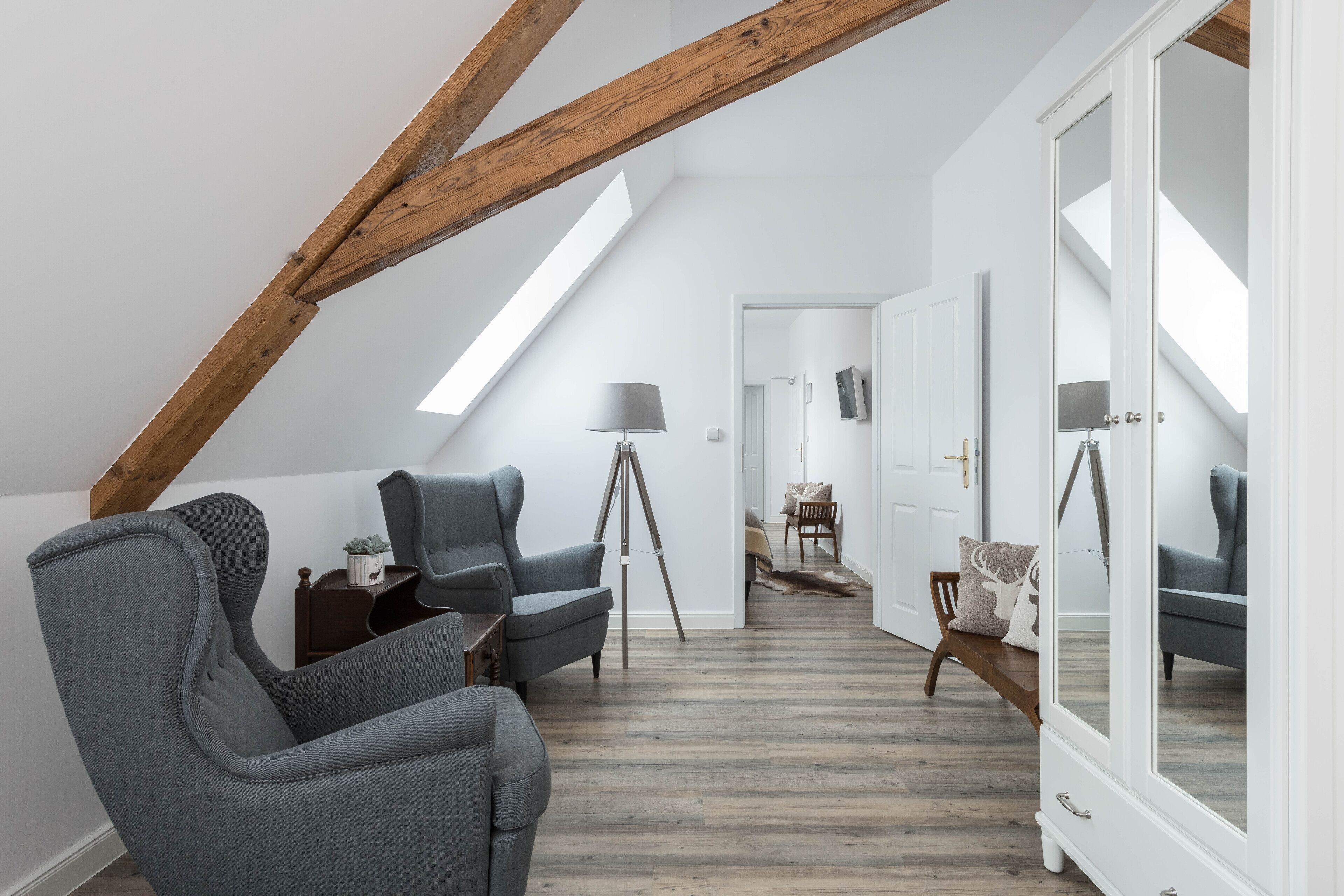 Un dormitorio tipo loft moderno con vigas de madera a la vista, tragaluces, un amplio armario y una zona de estar acogedora con una lámpara.