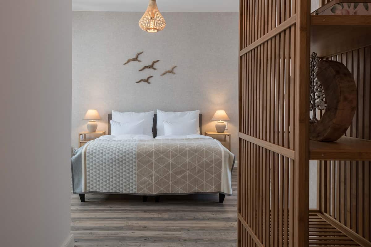 A bedroom with a bed, two bedside lamps, a wall-mounted bird decoration, and a wooden shelf with a decorative item.