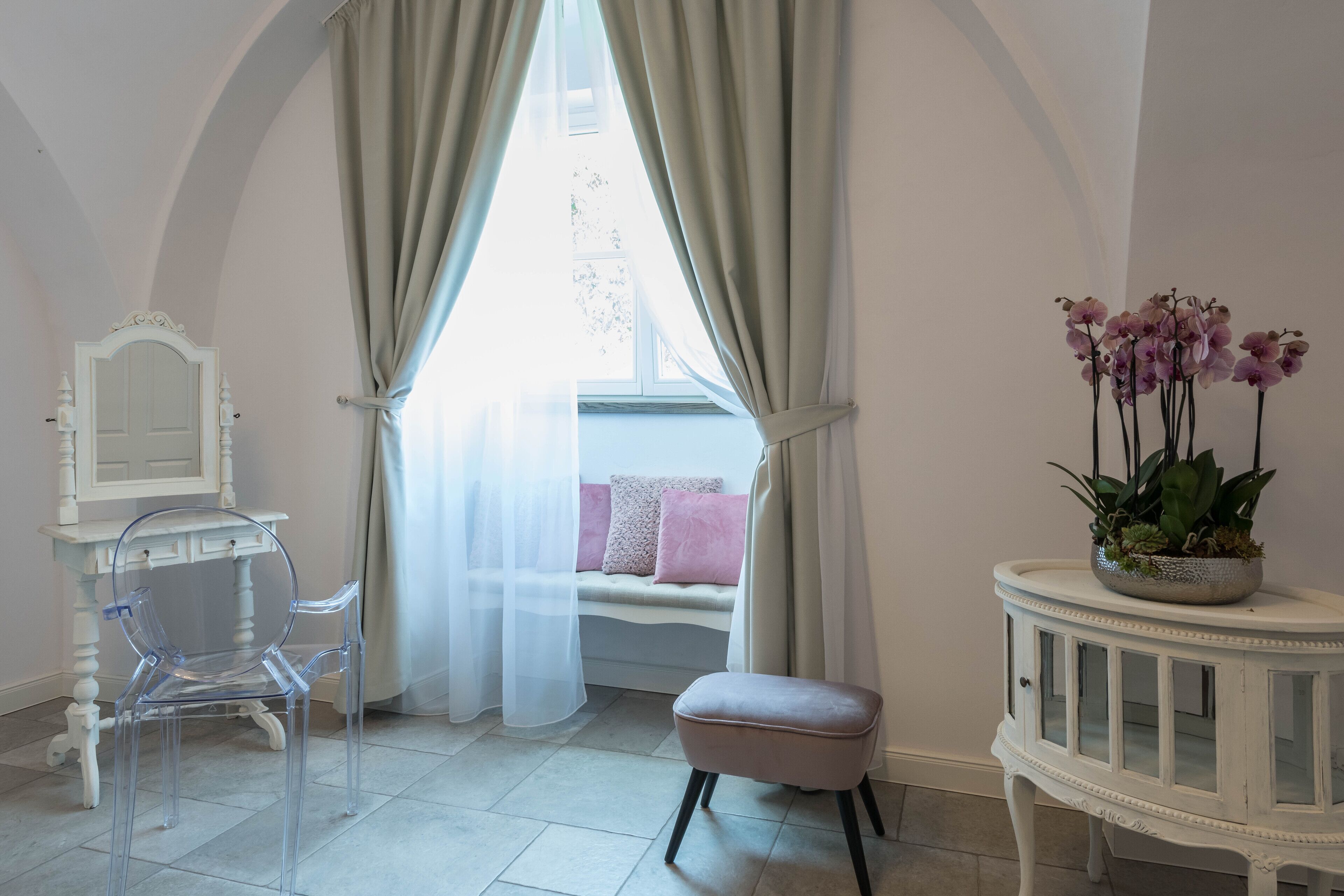 Een kamer met een transparante stoel, een kaptafel met spiegel, een comfortabele bank en een tafeltje met orchideeën.