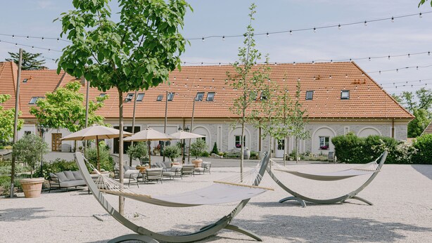 A courtyard with hammocks, outdoor seating, and a building with a tiled roof. - Na Kmíně (Obríství)