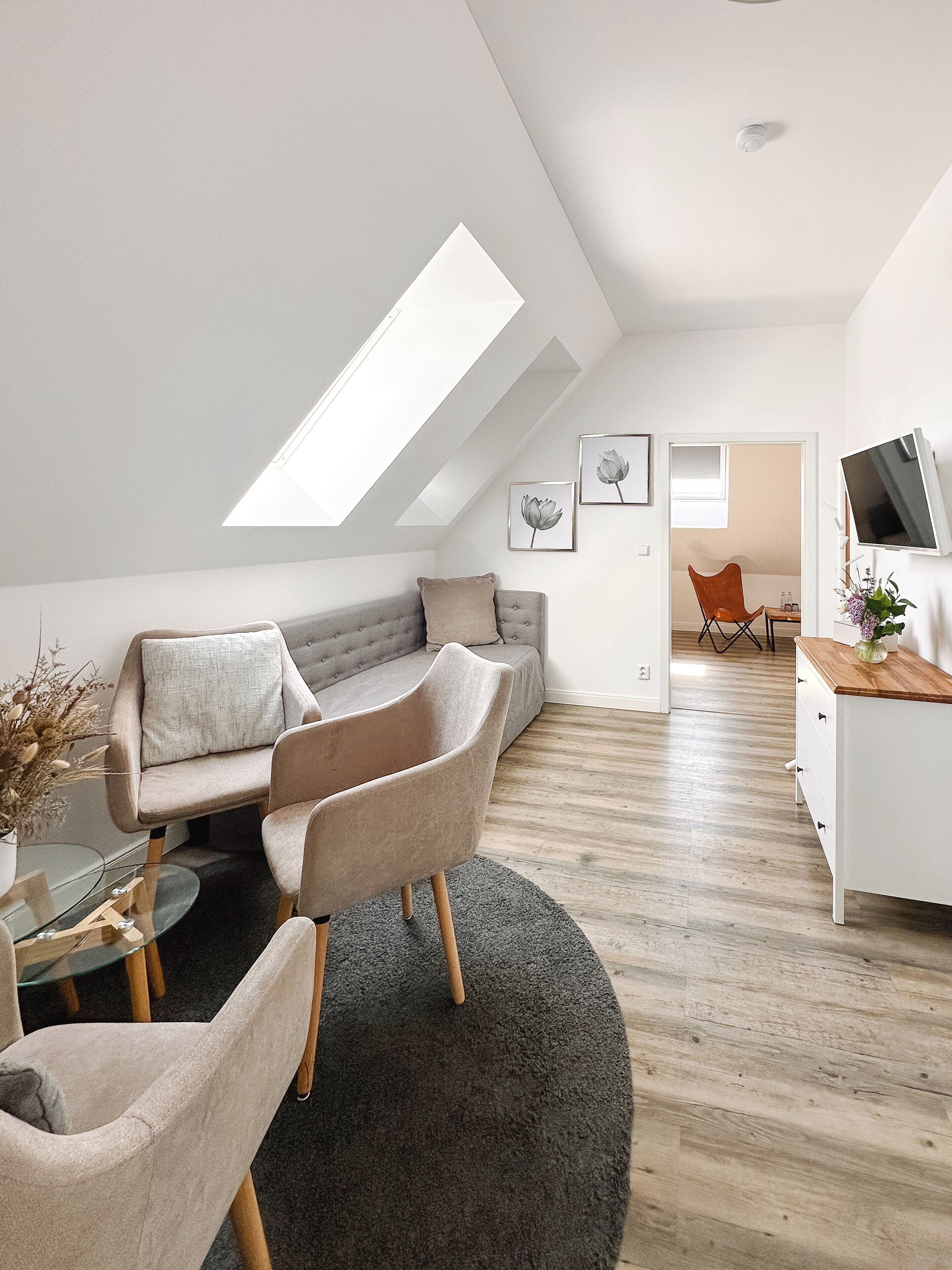 A modern loft apartment with a sloped ceiling, a grey sofa, a round coffee table, and a TV on a wooden stand.