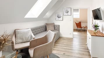 A modern loft apartment with a sloped ceiling, a grey sofa, a round coffee table, and a TV on a wooden stand.